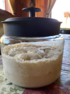 A bubbly liquid of sourdough starter in a glass jar with a black lid