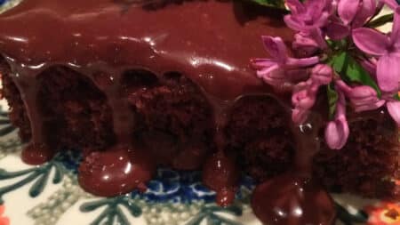 A decadent chocolate cake with a layer of glistening chocolate ganache, garnished with purple flowers.